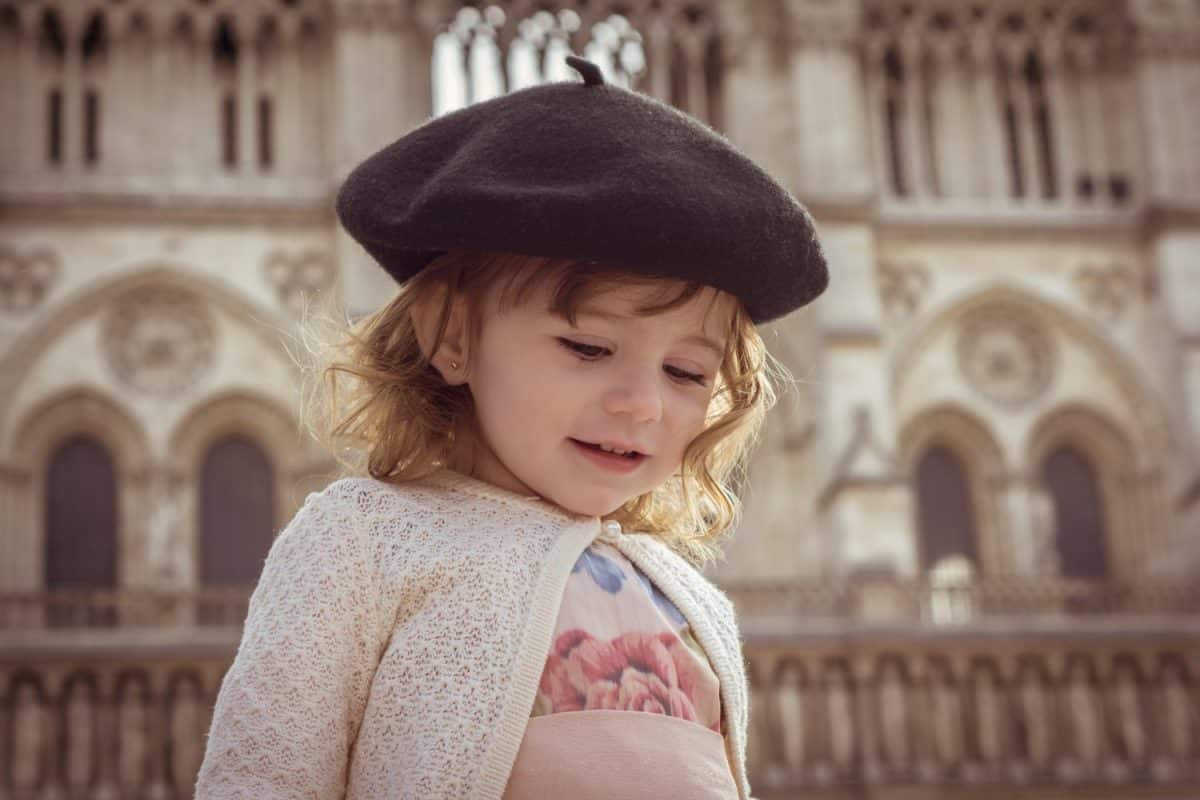 Sweet little baby girl (one year) with beret playing with doves in the cathedral of Notre Dame, Paris , France. Traveling with children. Beautiful and elegant pink dress and beret