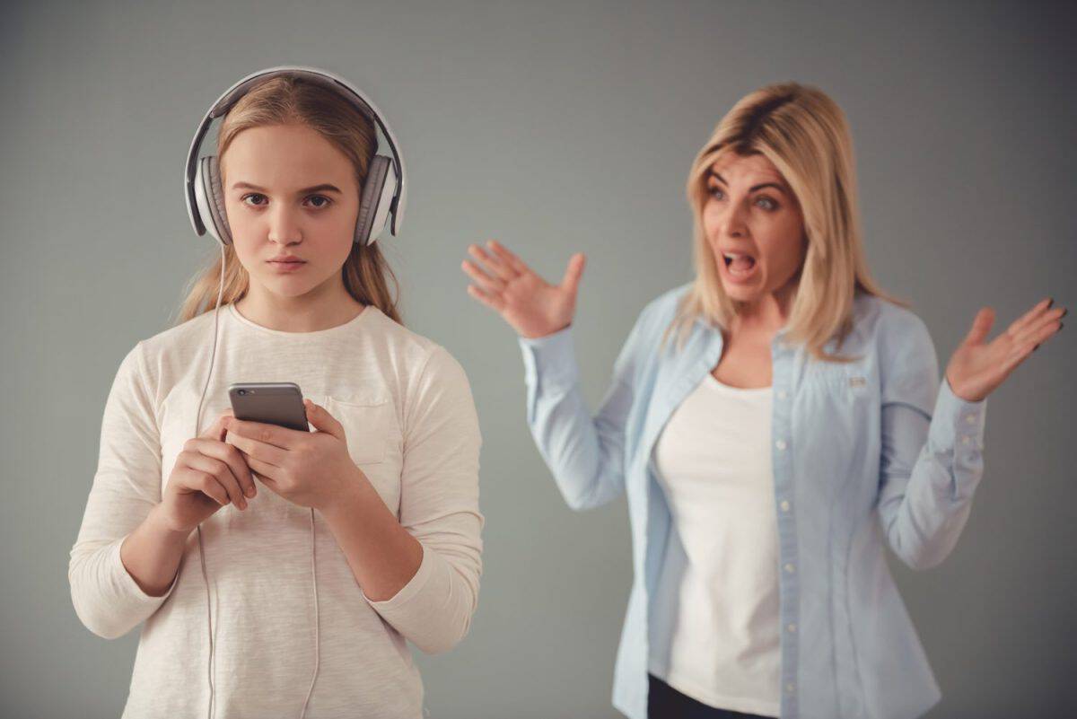 Beautiful woman is scolding her teenage daughter, girl is listening to music in headphones and ignoring her mom, on gray background