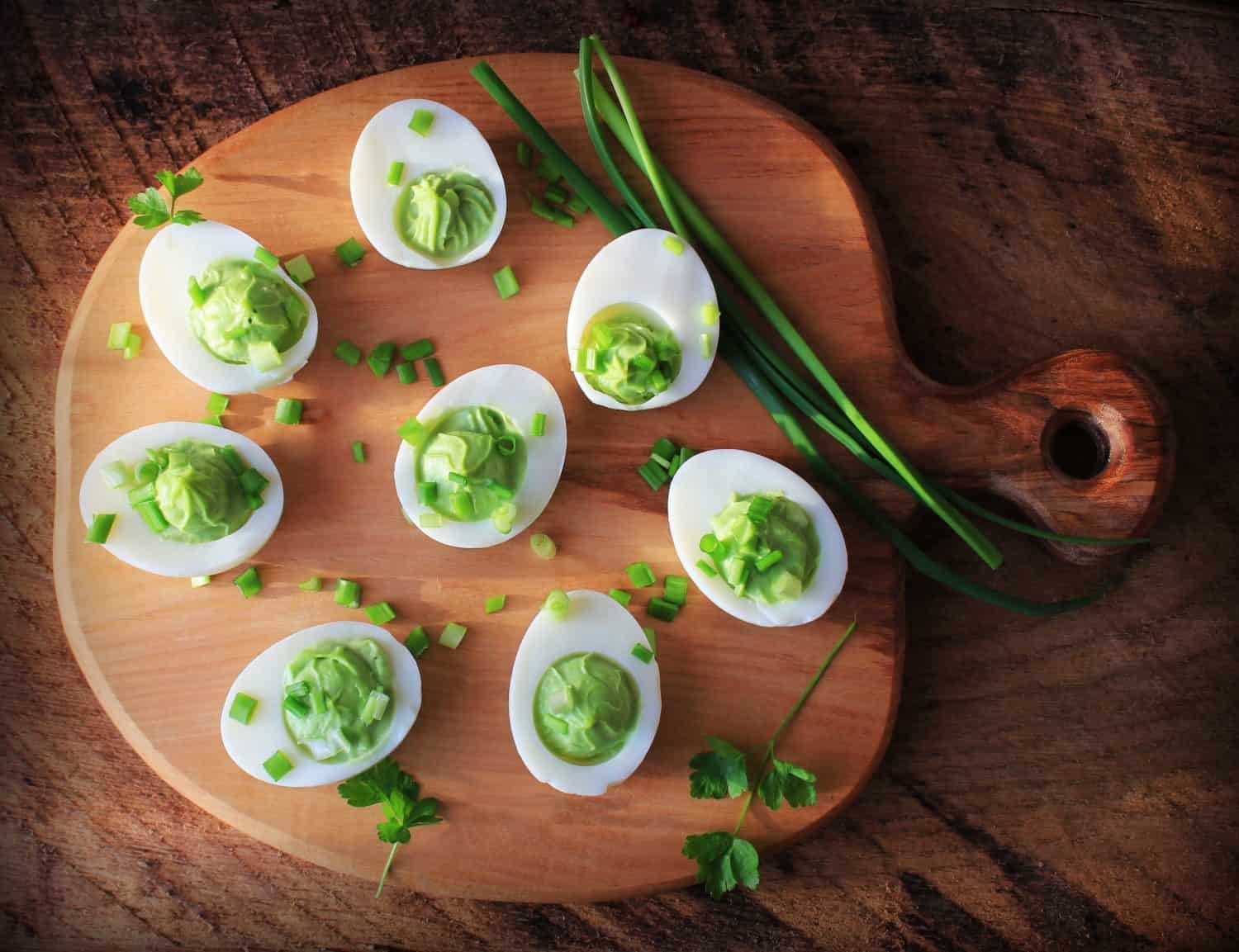 Deviled eggs appetizer with avocado on cutting board. Top view.