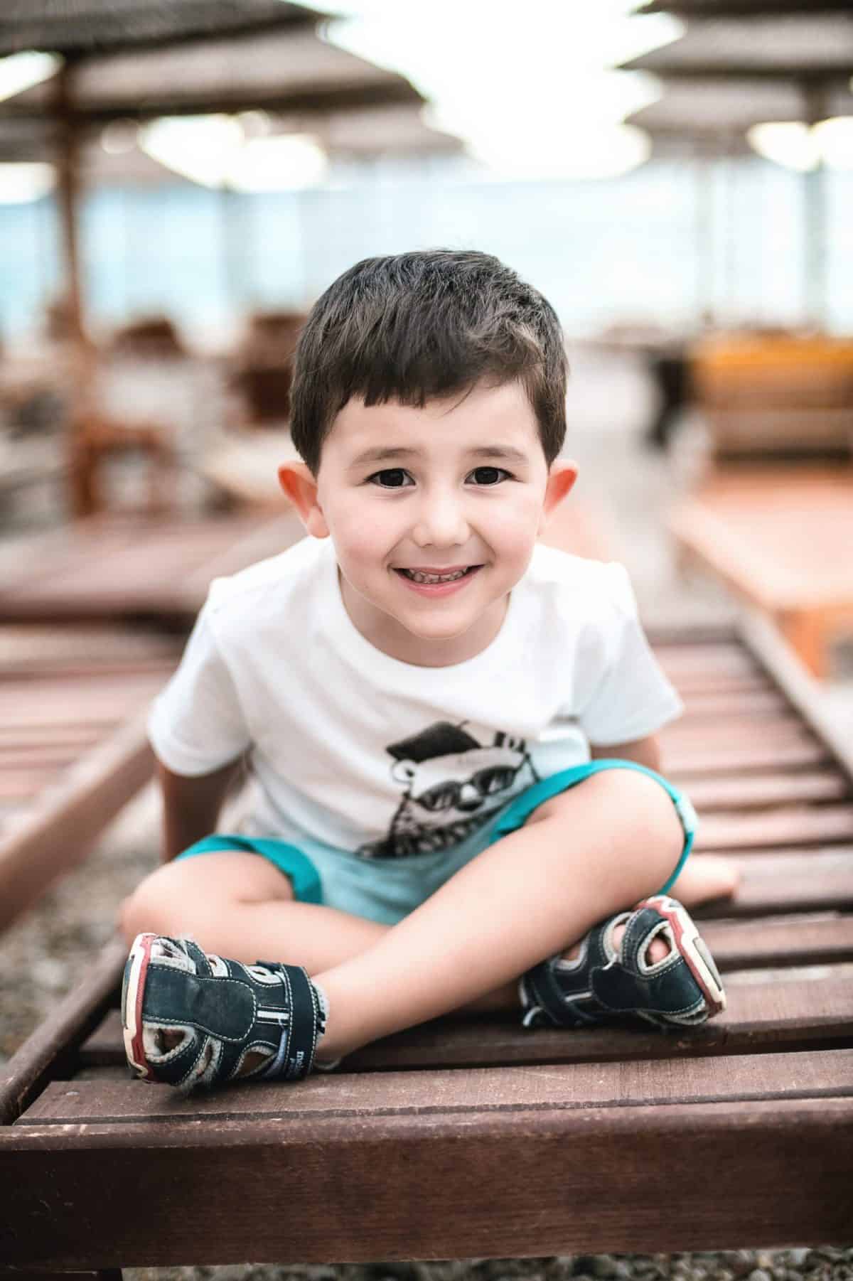 Cute little boy sitting crisscross on the beach in summer in Albania.