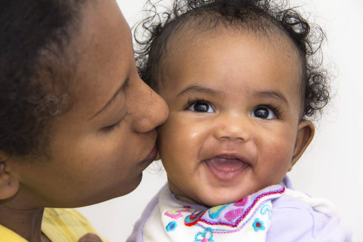 A mother kissing her smiling baby girl on the cheeks