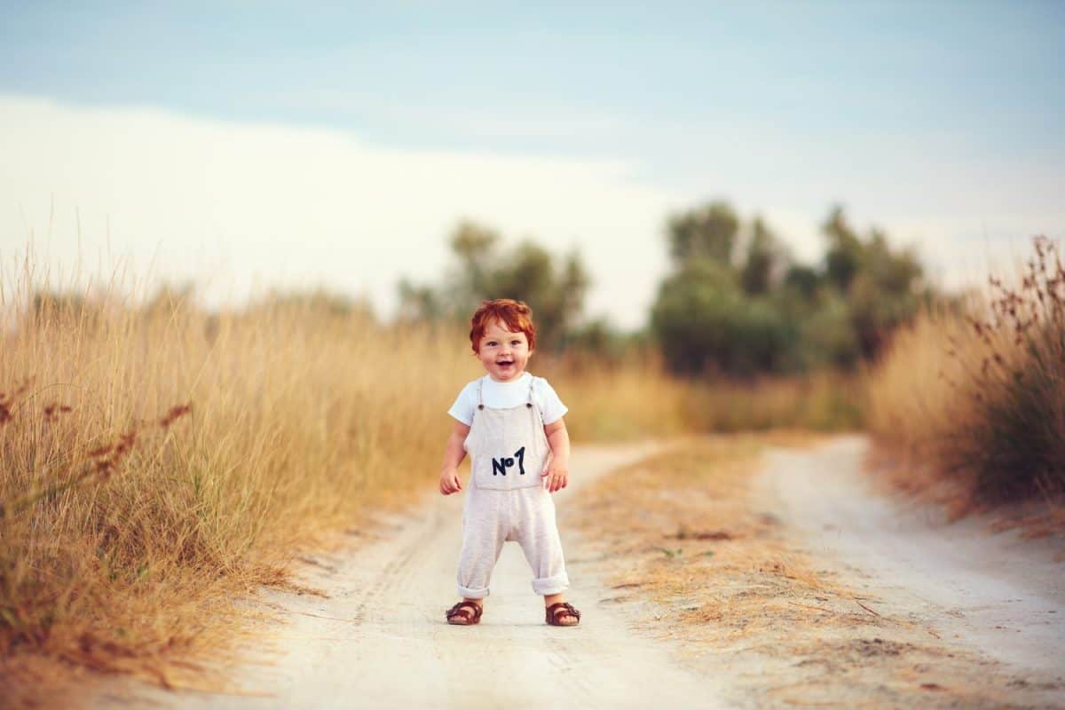 cute toddler baby boy having fun playing on the path at summer field