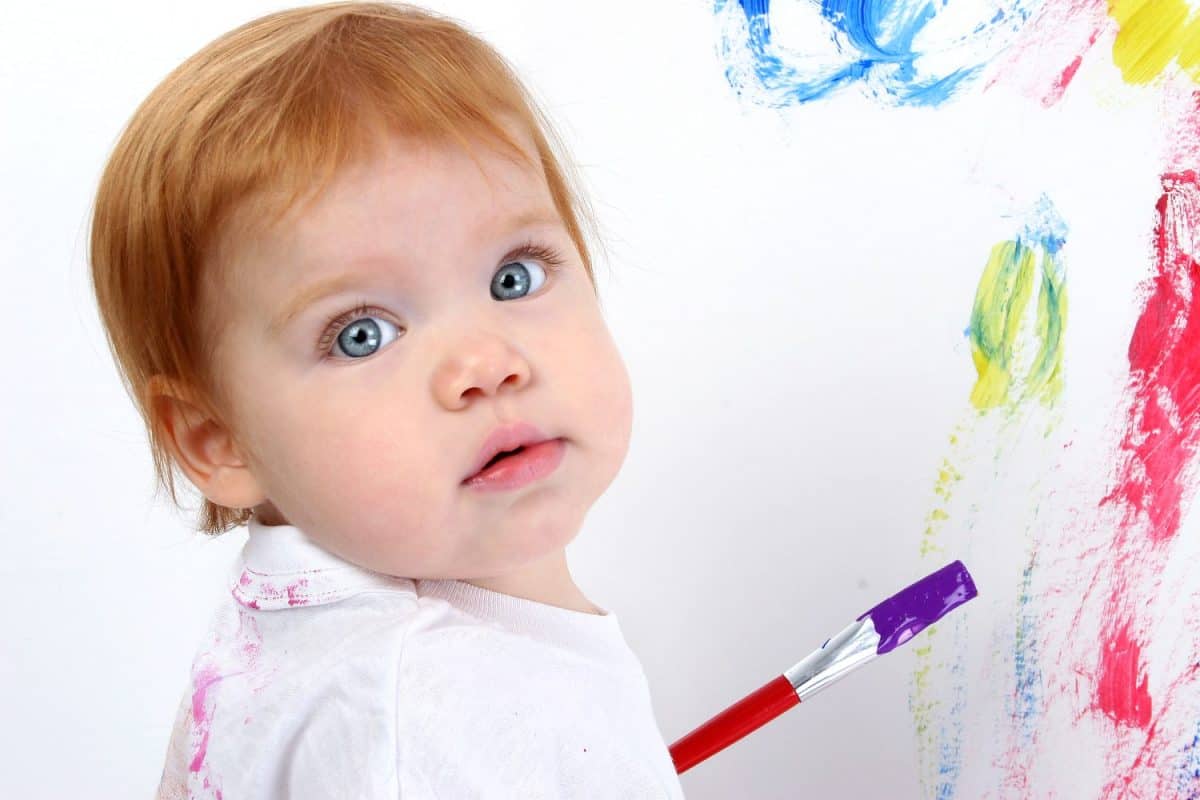 Beautiful little redhead baby painting at poster board. Bright blue eyes and red hair. Shot in studio.