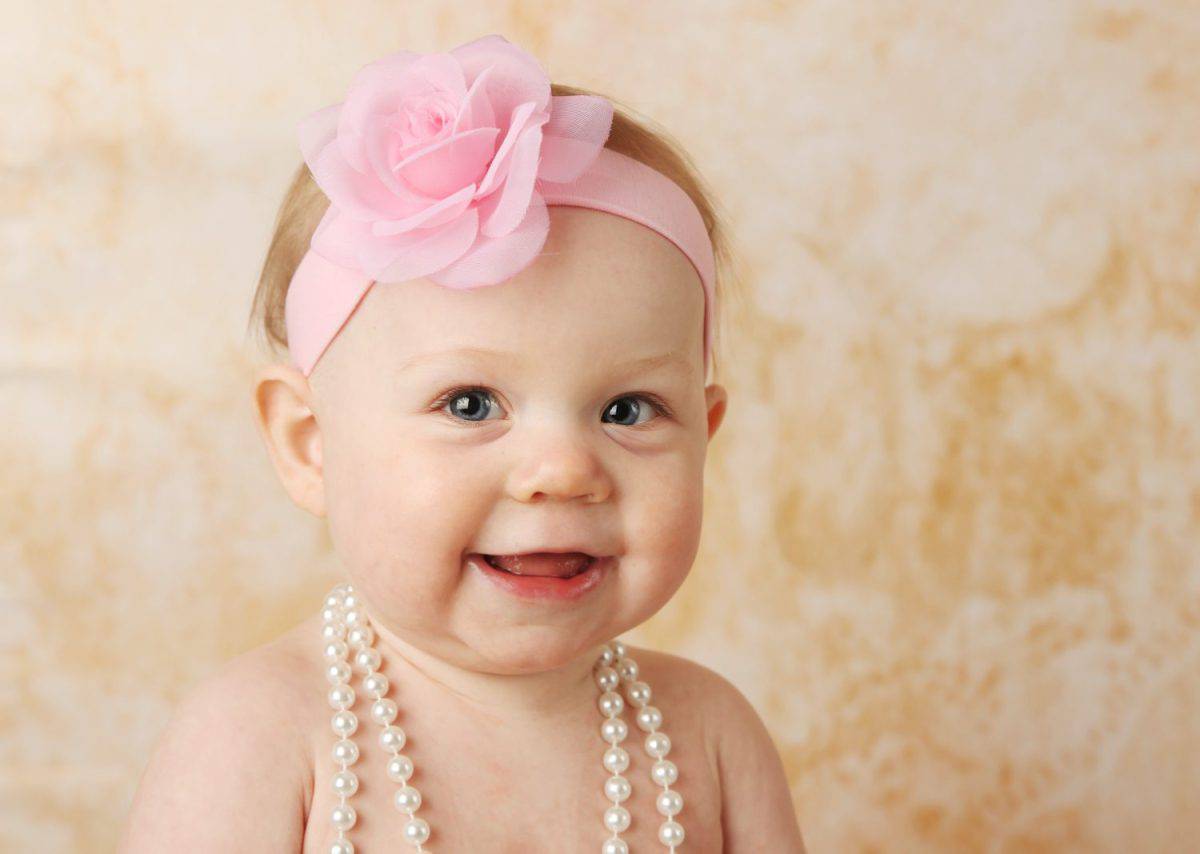 Adorable young baby girl wearing a vintage pearl necklace and pink rose headband