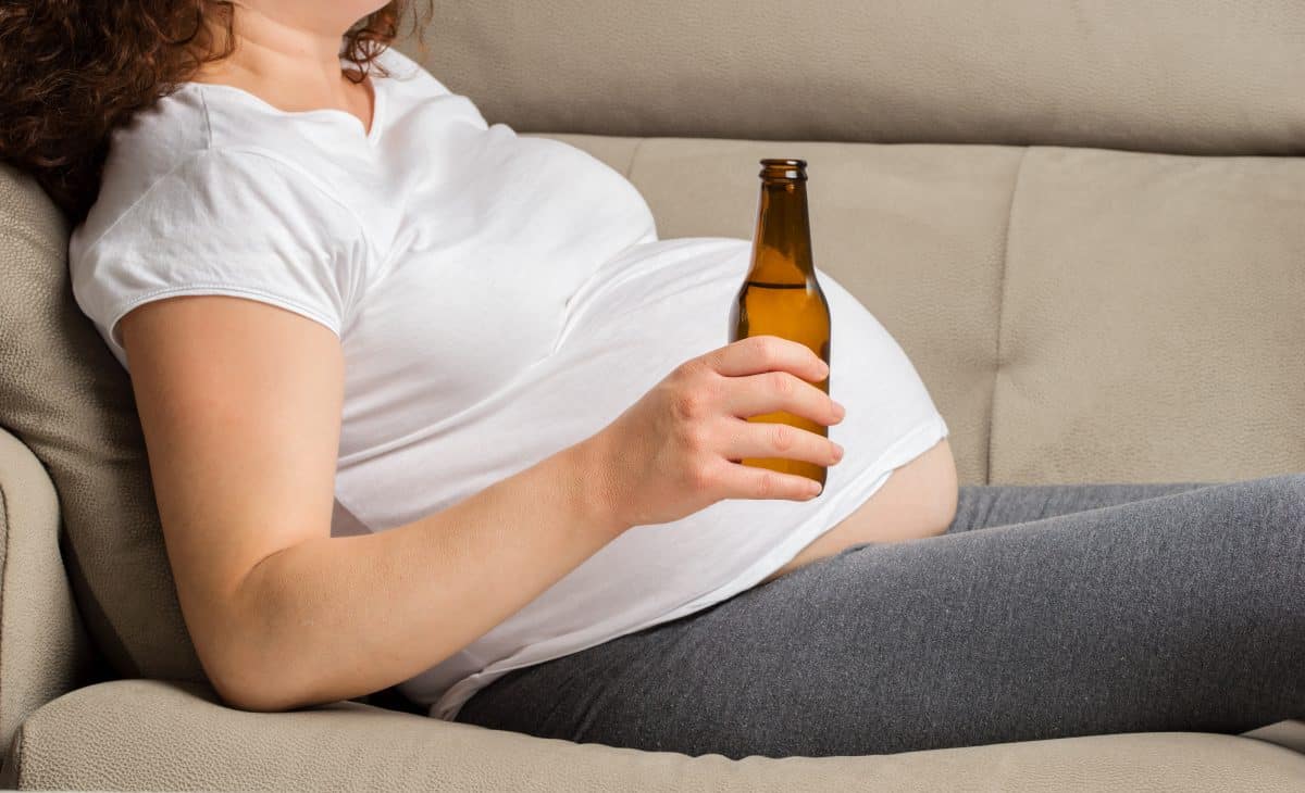 Shot of a woman drinking wbeer while preganant at home