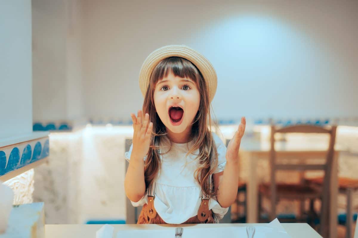 Funny Girl Screaming with Happiness in a Restaurant. Happy little child having a sense of humor and a loud voice