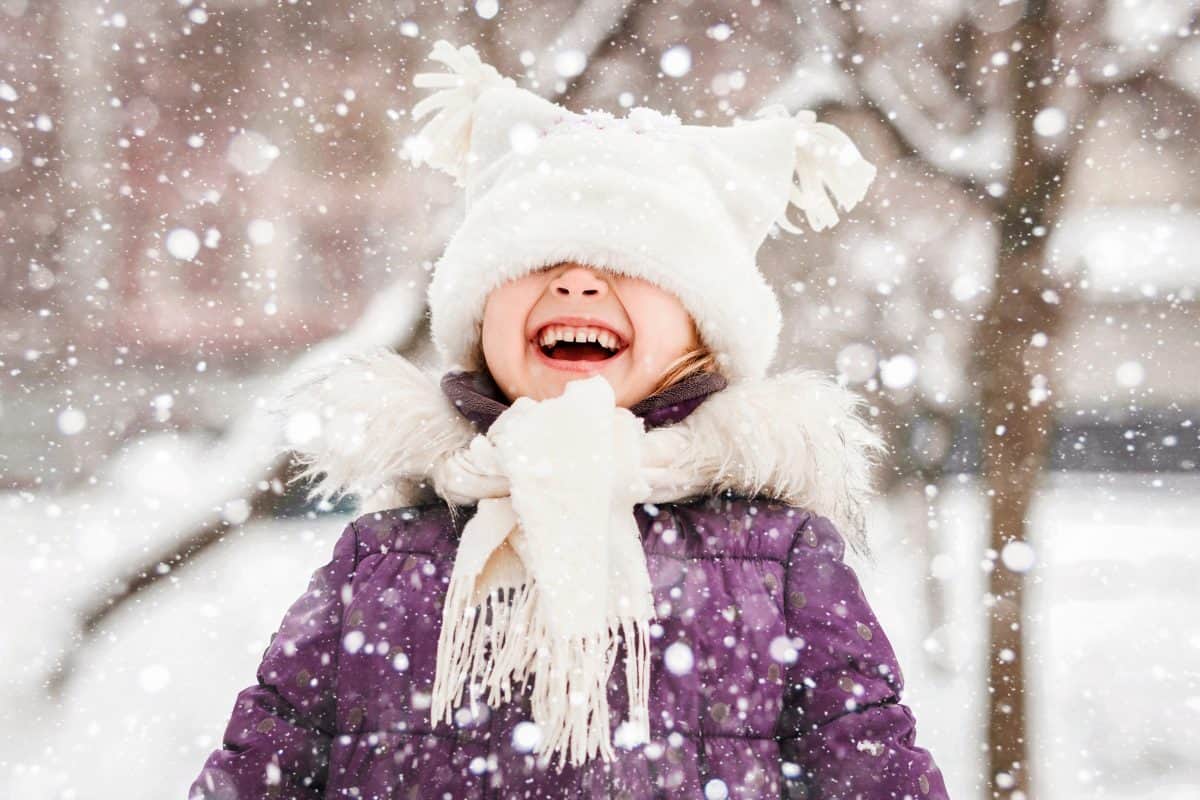 Happy Winter Children Holidays. Emotional Smiling Little Girl Child Having Fun Playing with Snowflakes in Winter Snow Park. Snow Falling in Winter Vacations.