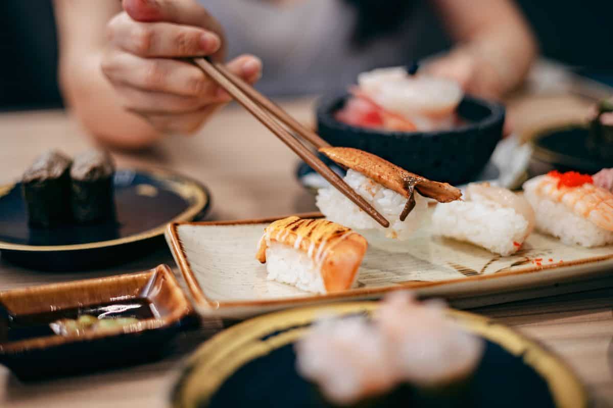 Close up shot of young Asian woman eating fresh nigiri sushi with chopsticks, served with miso soup and salad on the side in a traditional Japanese restaurant. Asian cuisine and food concept.