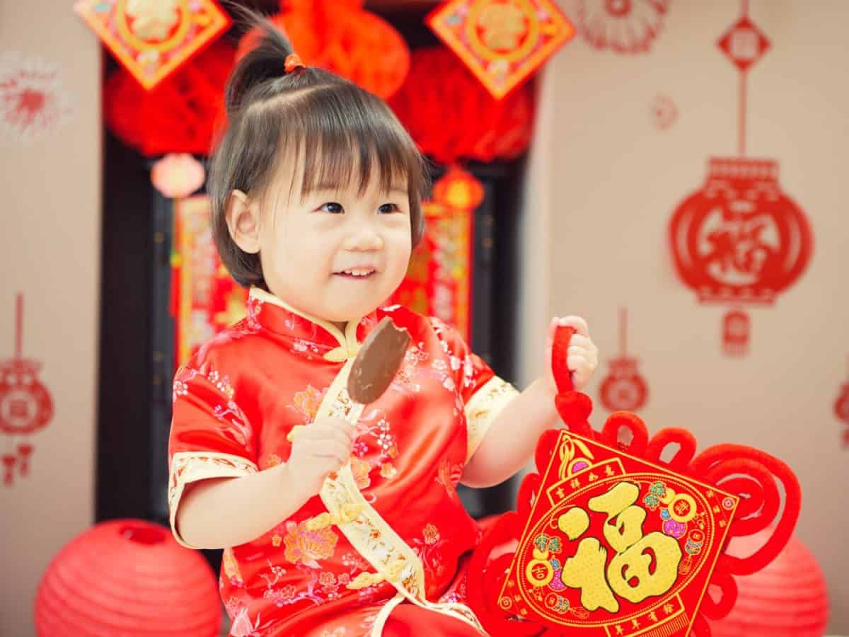 Chinese baby girl with traditional dressing up and "FU" means "lucky" greeting card.some "FU" means "lucky"greeting card on the wall as well