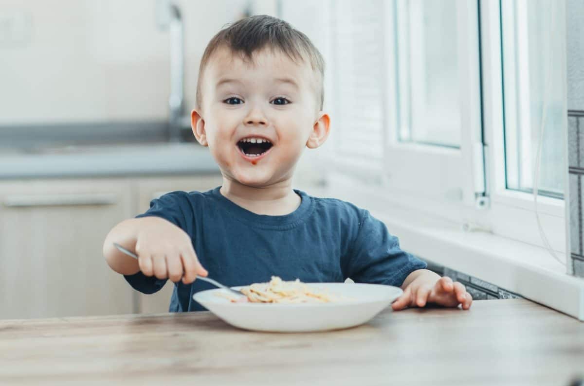 The child in the kitchen at the table eating macaroni and interesting view from the top