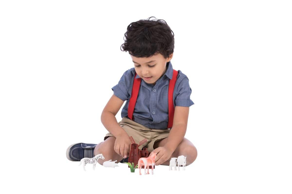 A little baby boy sitting on the floor playing with plastic animals, isolated on a white background.