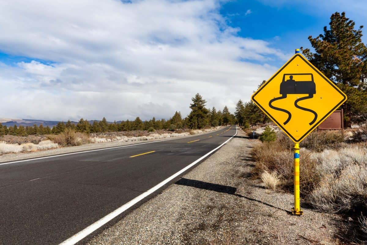 A slippery when wet road sign on the right side of the route 120 that winds through the Eastern Sierras around Mono Lake area warns drivers to be careful when driving.