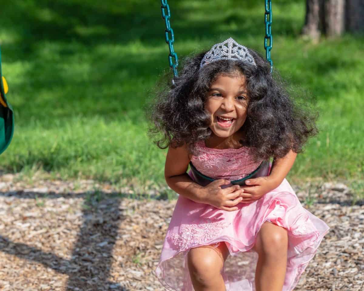 A smile todler is trying to sit on the swing at the playground