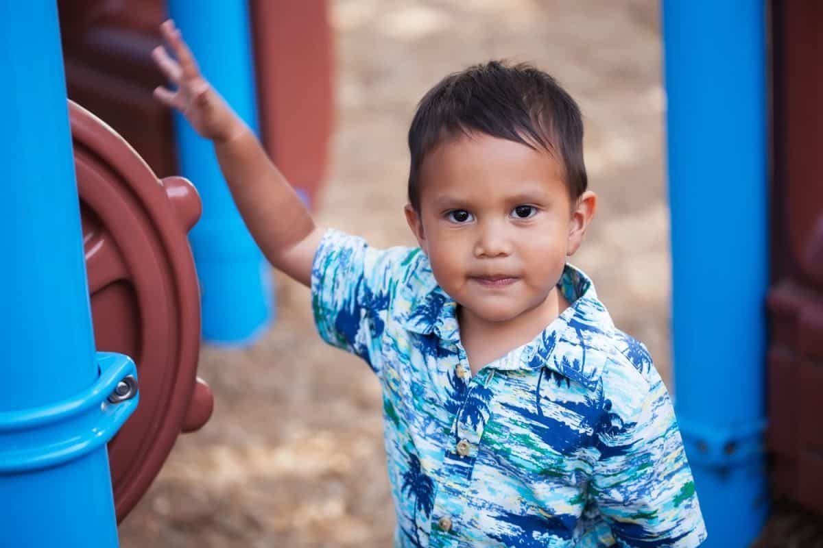 Young male boy spinning the helm of a toy ship in a kids playground with confidence.