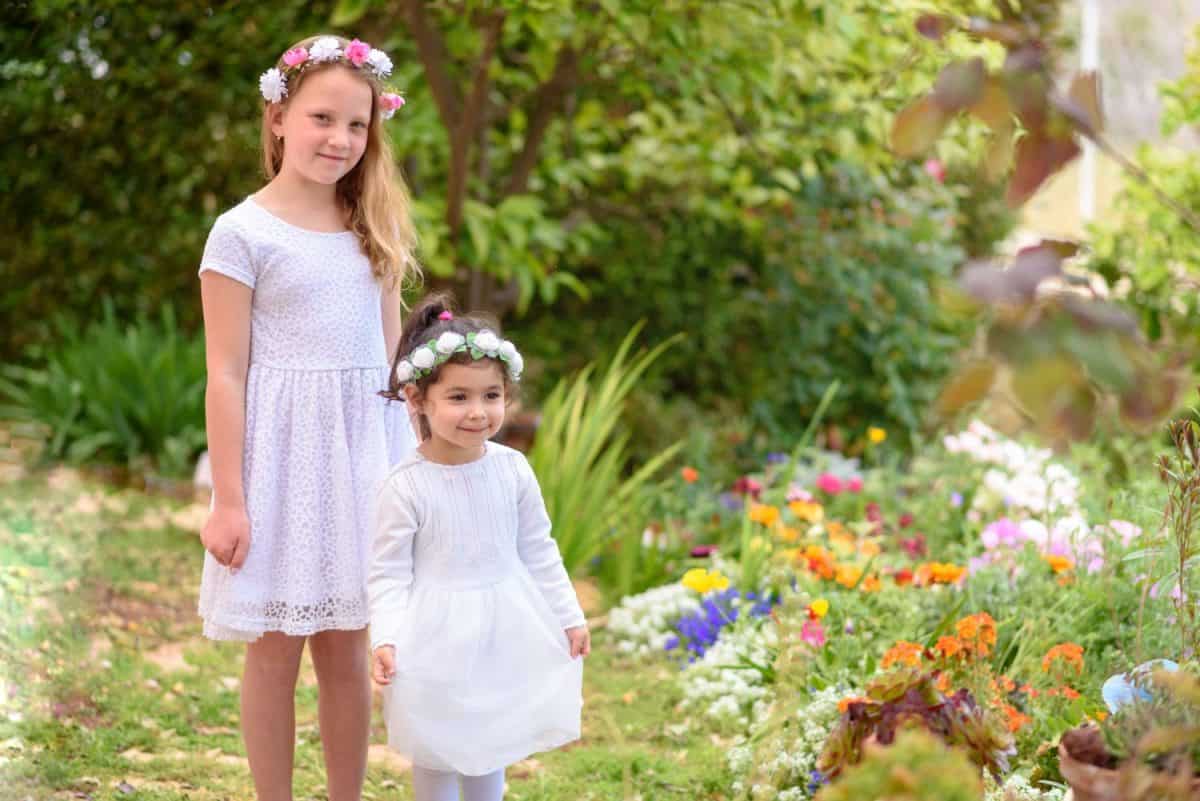 Two happy multiracial children with white dress and flower wreath playing outdoors. Kids having fun in summer or spring park. Beautiful girls on colorful nature background.