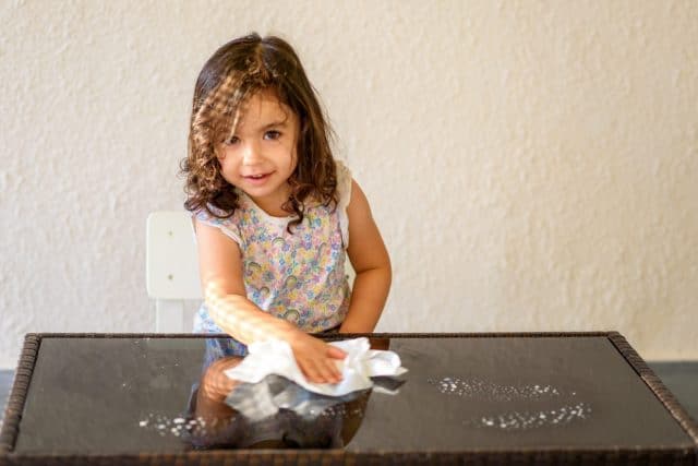 Cute child help mom cleaning glass table. Little girl make cleaning in room at home.