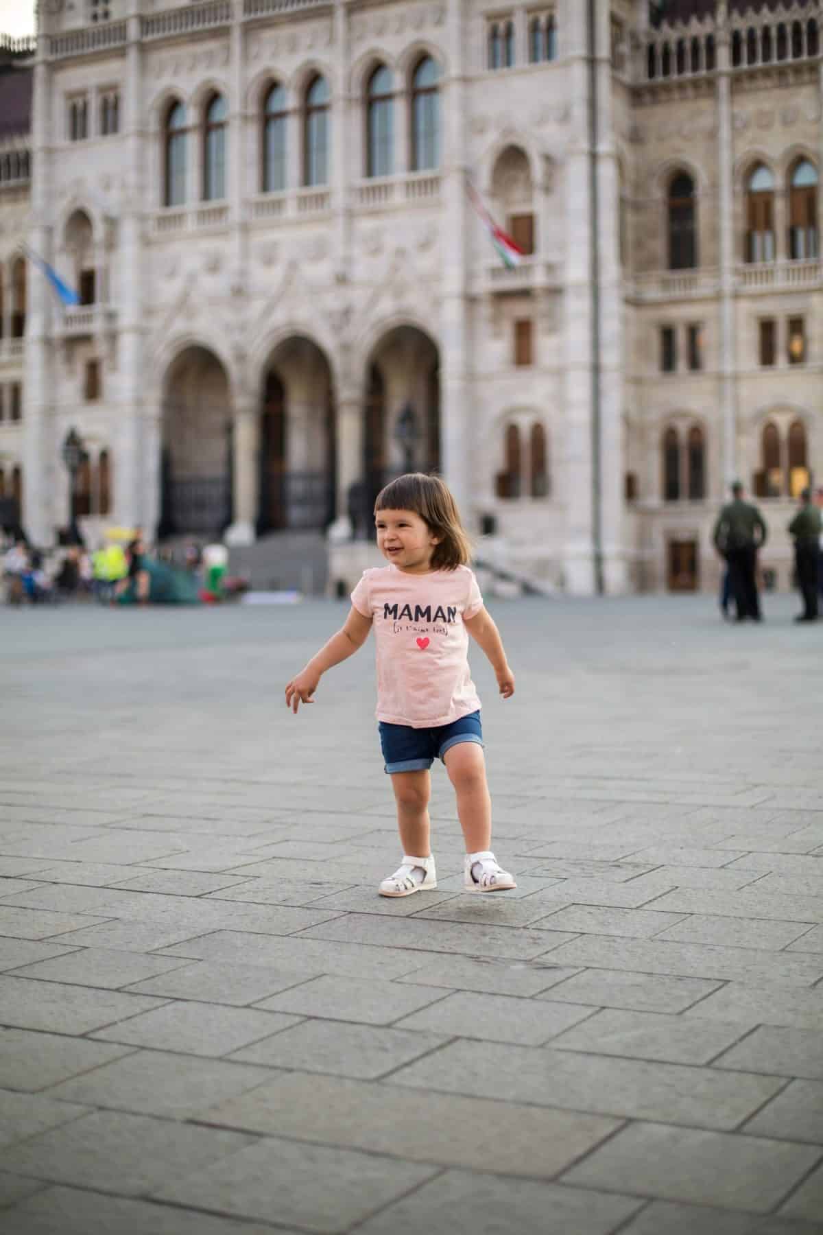 little girl child in shorts and a t-shirt stands near the Hungarian Parliament in Budapest