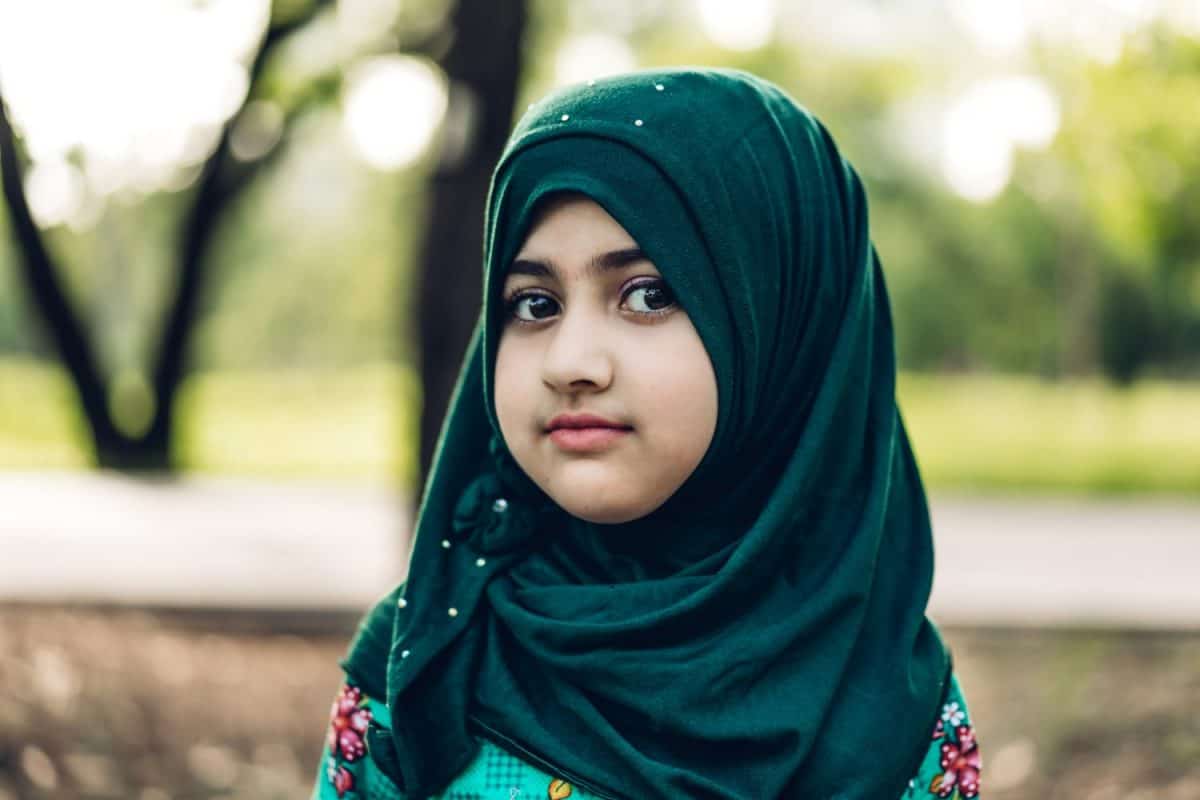 Portrait of happy little muslim girls child with hijab dress smiling and looking at camera in the park