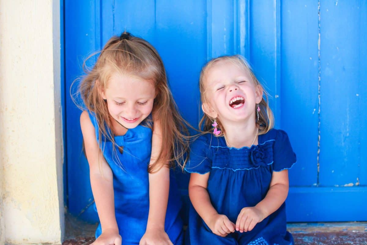 Portrait of Little smiling girls sitting near old blue door in Greek village, Emporio, Santorini