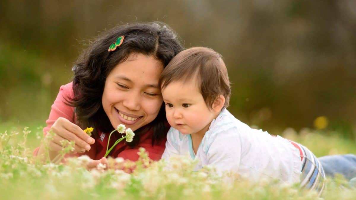 Happy Filipino Mother and Baby half Filipino Daughter playing and laying in a green field