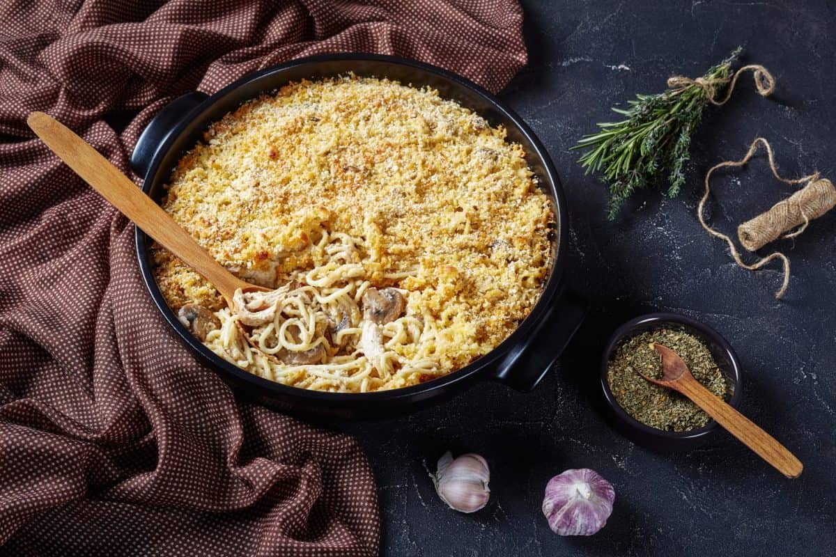 close-up of roasted turkey breast tetrazzini with breadcrumbs crust in a black backing dish with a wooden spoon on a concrete table, american cuisine, horizontal view from above