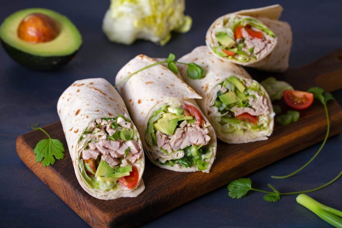 Turkey wraps with avocado, tomatoes and iceberg lettuce on chopping board. Tortilla, burritos, sandwiches, twisted rolls