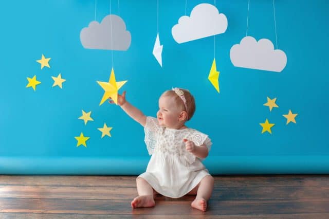 One year old baby celebrates birthday. Photo zone. Cute dress in white color. She touches a paper yellow star.