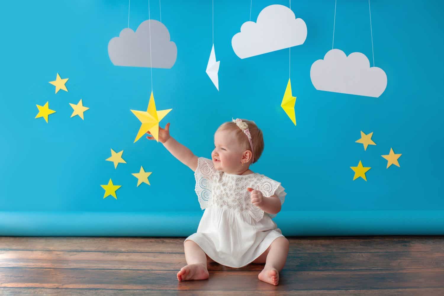 One year old baby celebrates birthday. Photo zone. Cute dress in white color. She touches a paper yellow star.