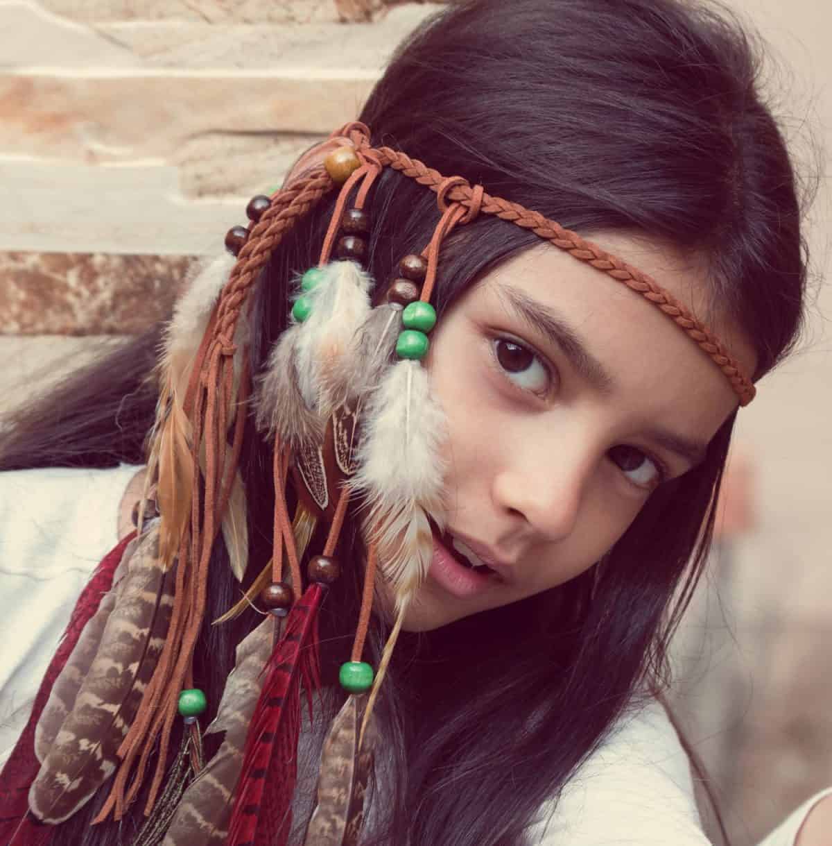 Little girl playing dress-up as Native American, wearing Indian headdress. Cute little girl playing in teepee. Boho style.