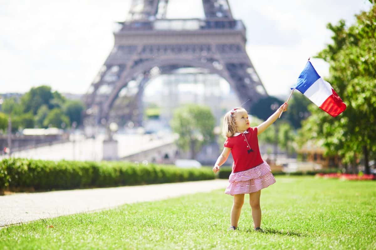 Beautiful toddler girl with French national tricolor flag near the Eiffel tower in Paris, France. 14 July (Bastille day), main French national holiday