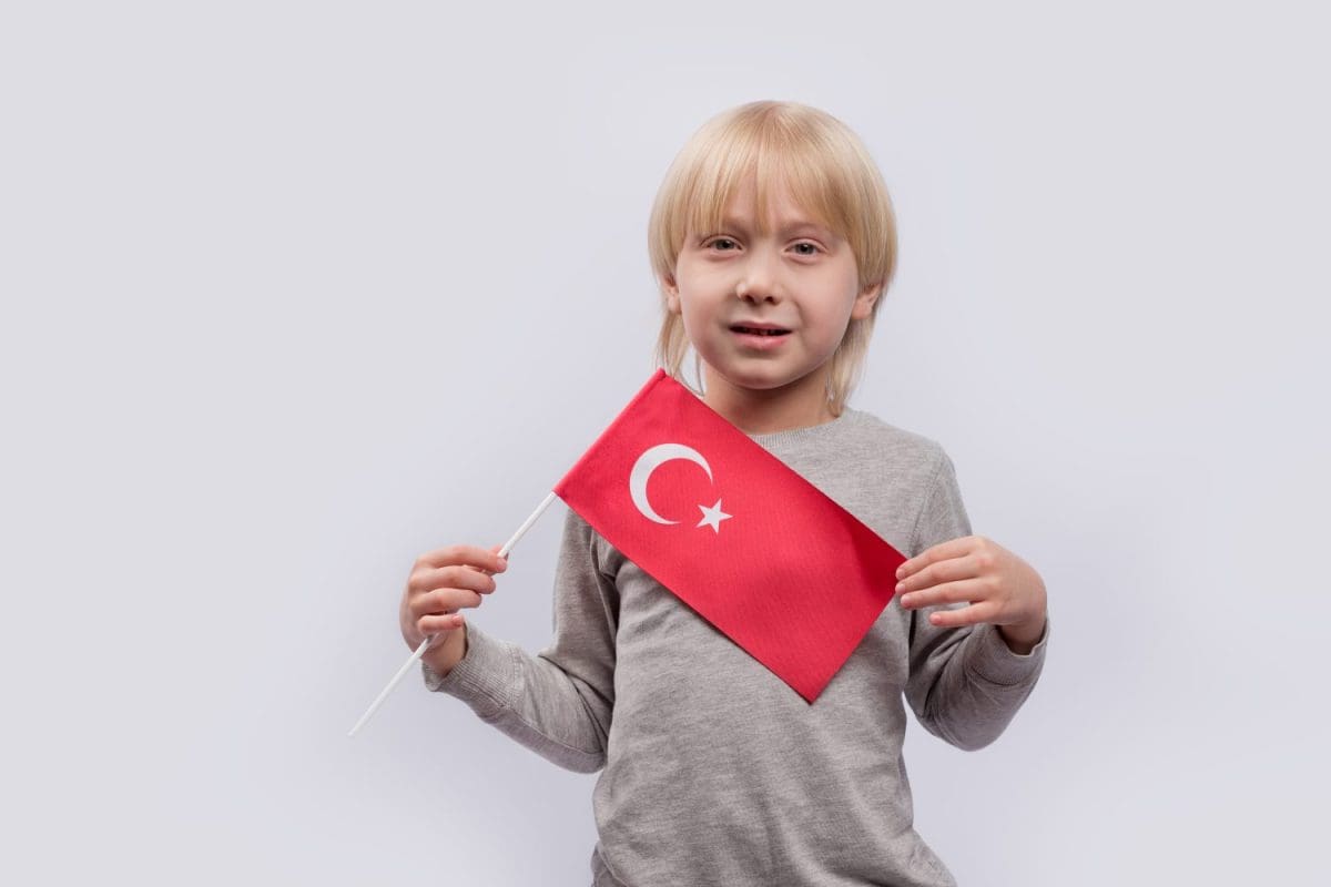 Cute blonde boy holds Turkish flag on white background. Children's education in Turkey.