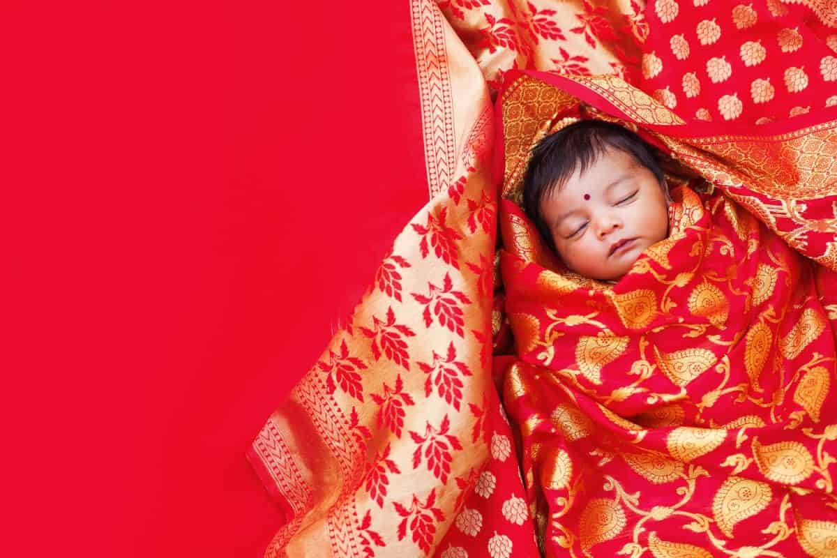 Beautiful Indian newborn baby girl with bindi wrapped in a red banarasi saree sleeping