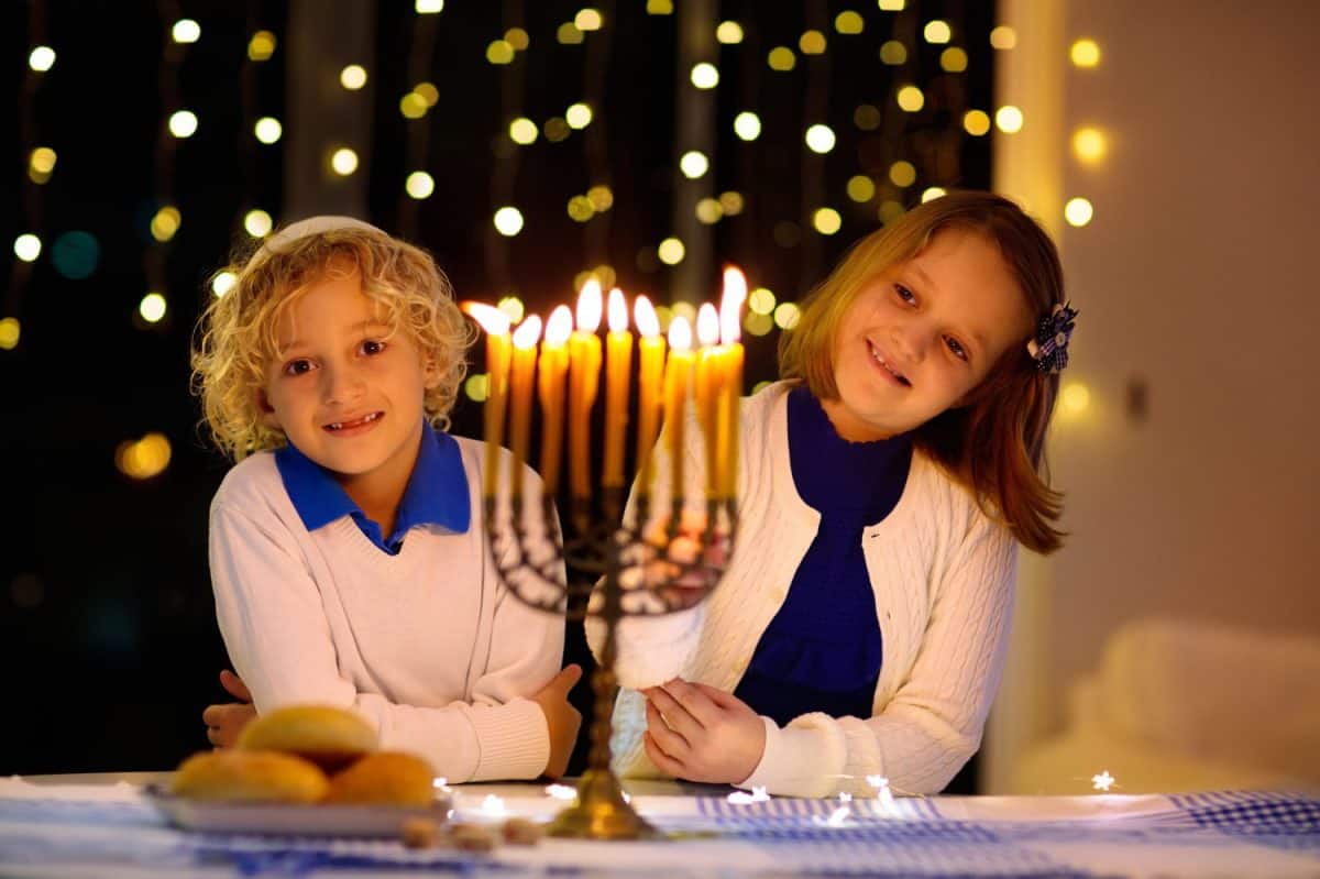 Kids celebrating Hanukkah. Jewish festival of lights. Children lighting candles on traditional menorah. Boy in kippah with dreidel and Sufganiyah doughnut. Israel holiday.