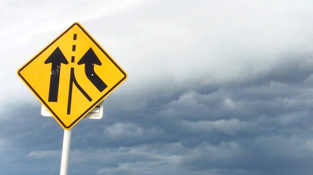 A yellow and black divided highway sign the clouds