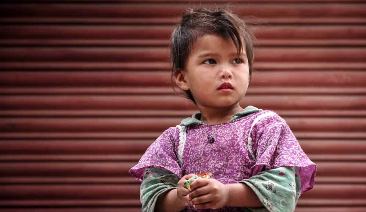 April 11, 2010, Kathmandu, Nepal. Young girl looking at her friend playing cricket in front of a closed shop