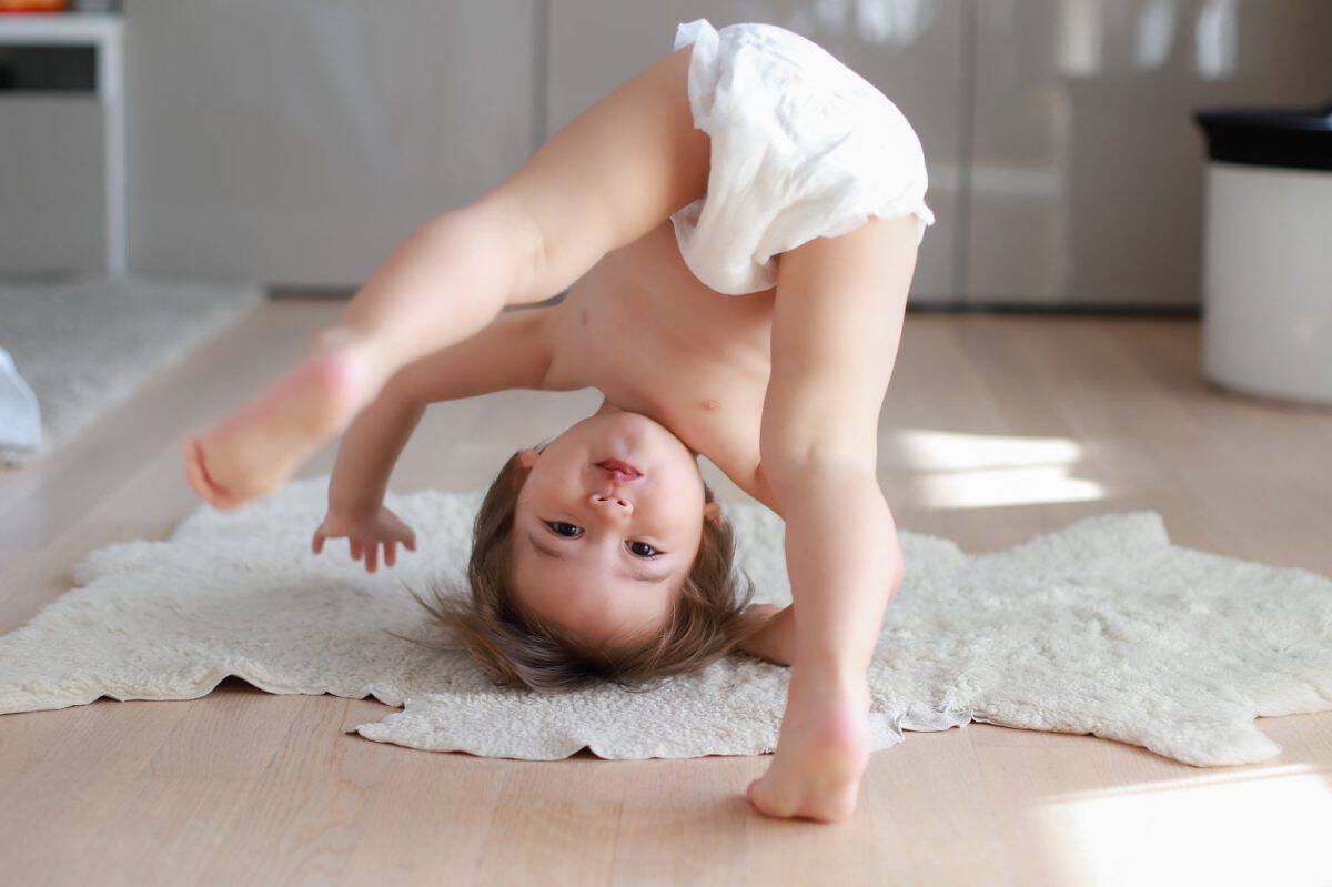 Cute and funny baby boy wearing diaper bending over doing yoga or playing hide and seek at home. Happy mixed race Asian-German child play and learn development.