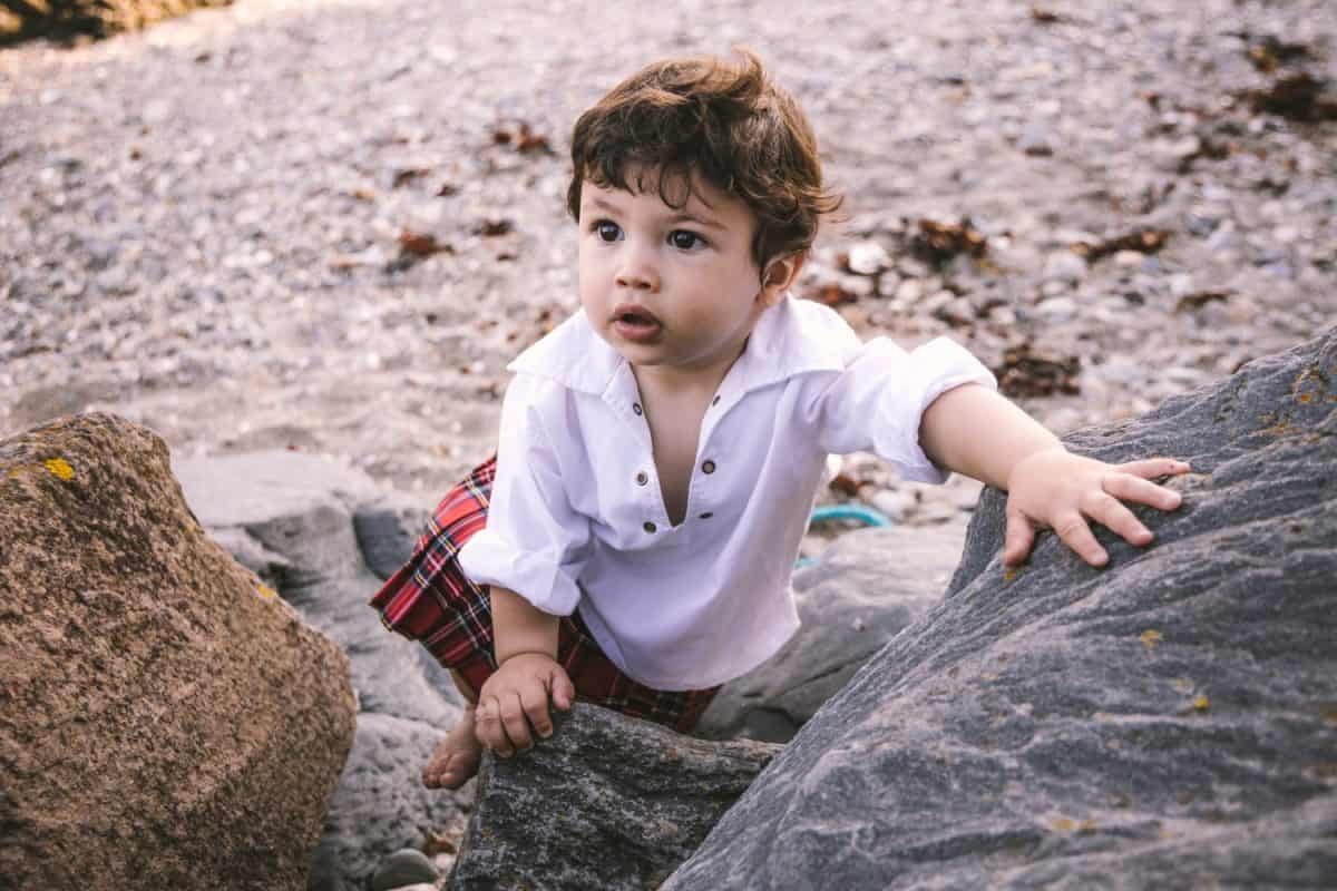 Baby boy in kilt climbing rocks