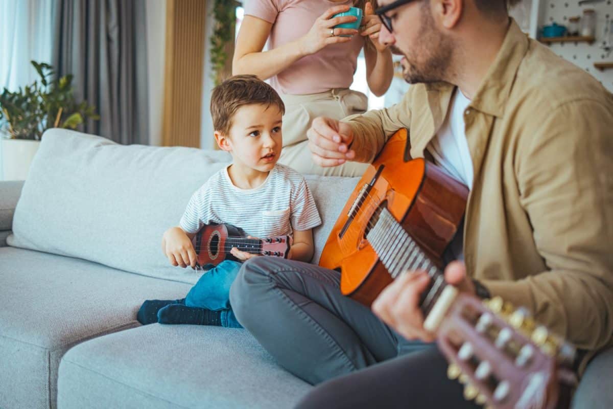 Single Father At Home With Son Teaching Him To Play Acoustic Guitar at home. Getting it right together. Shot of a boy learning to play guitar from his father