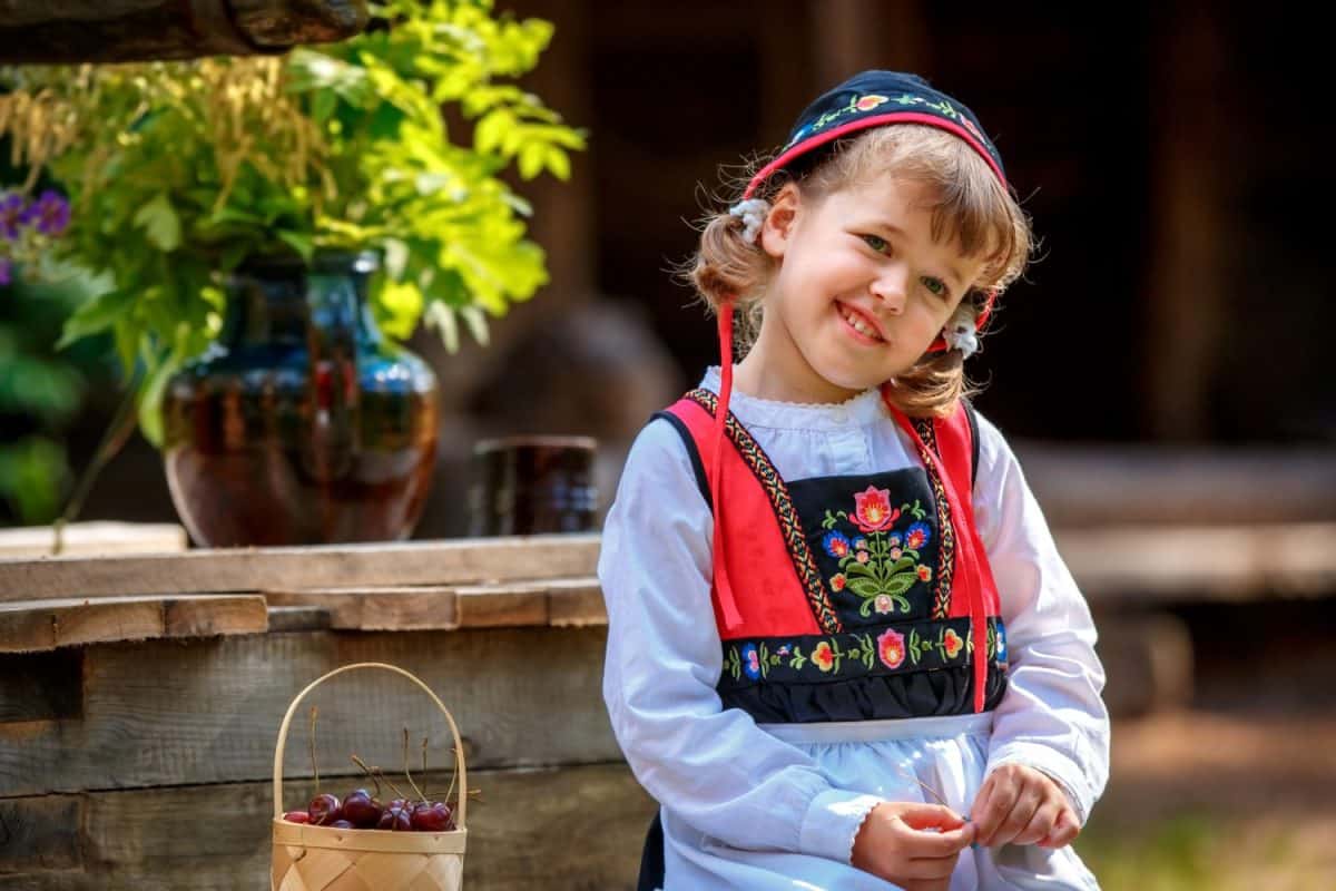 Adorable little girl in Swedish traditional clothes holding basket with cherries during Midsommar festival celebration