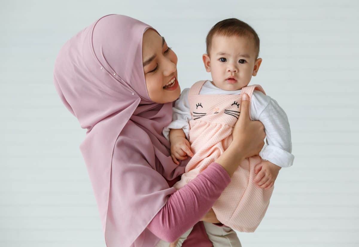 Portrait of a beautiful Muslim woman with a friendly and warm smile hugging and cuddling Muslim infant baby. They wearing colorful hijab traditional Islamic dress. Religious and fimily concept.