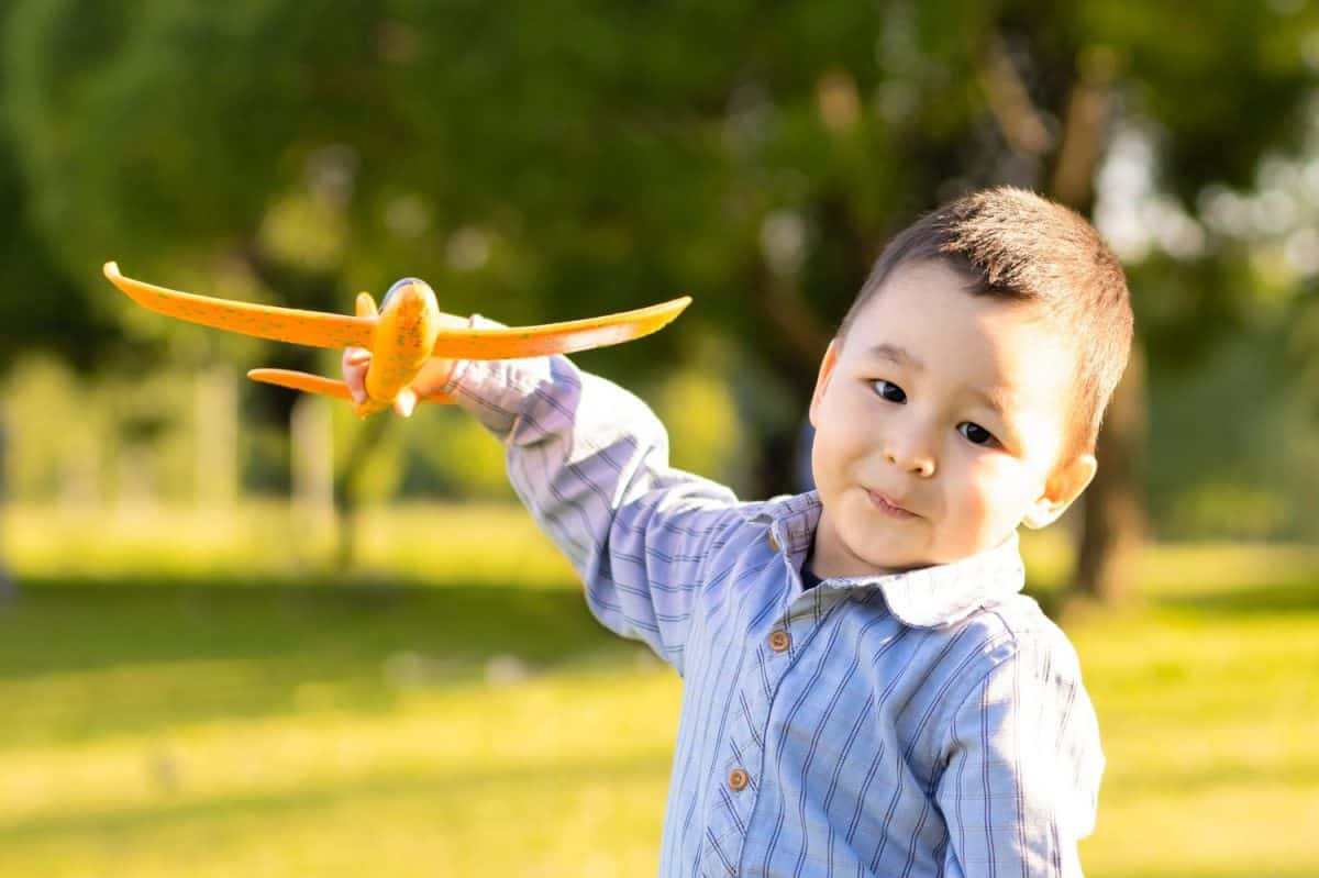 asian boy playing with toy plane in park. Muslim Kazakh child pilot flying airplane on field. islamic kid aviator dreaming, traveling. Imagination and motivation concept. Startup, freedom.