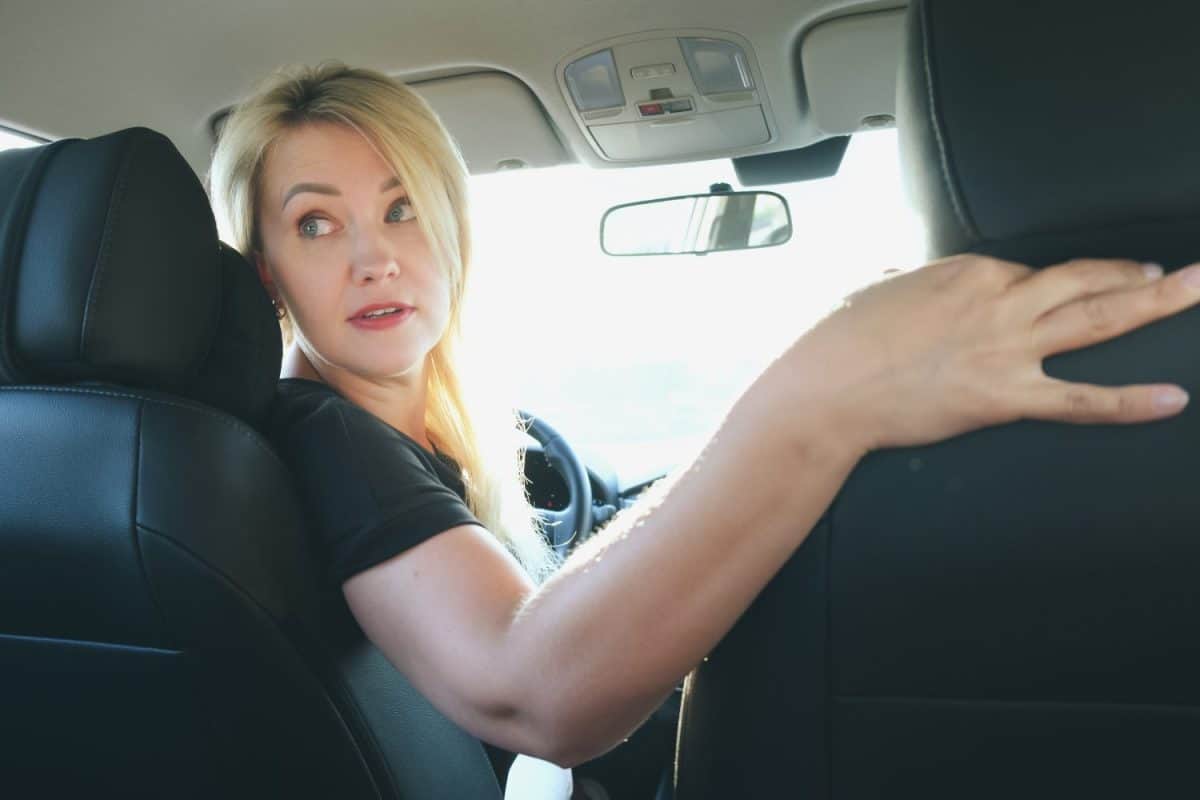 Attractive blonde woman driving a car turned around to look out the rear window. The woman behind the wheel backs up. Driving, parking.