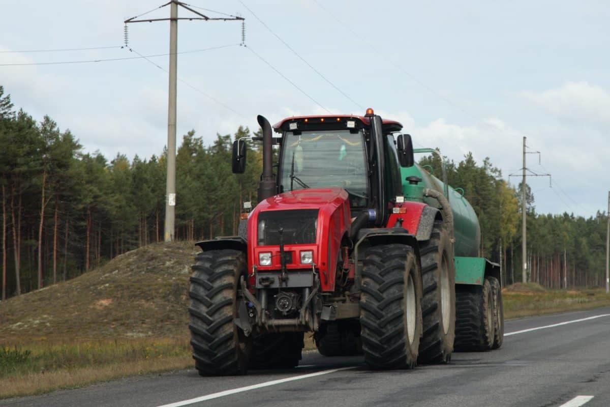 Big red wheeled tractor with barrel drive on country highway road