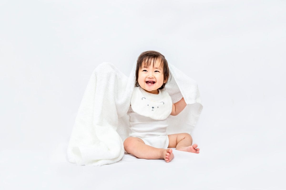 One baby girl sitting in front of white background covered bath towel and smiling