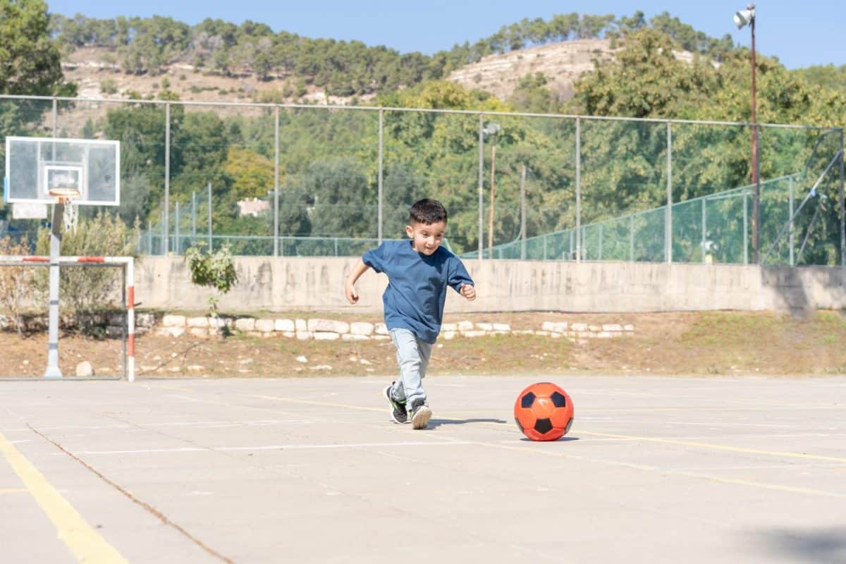 Cute Boy Running With Ball. Little Child Playing Football.