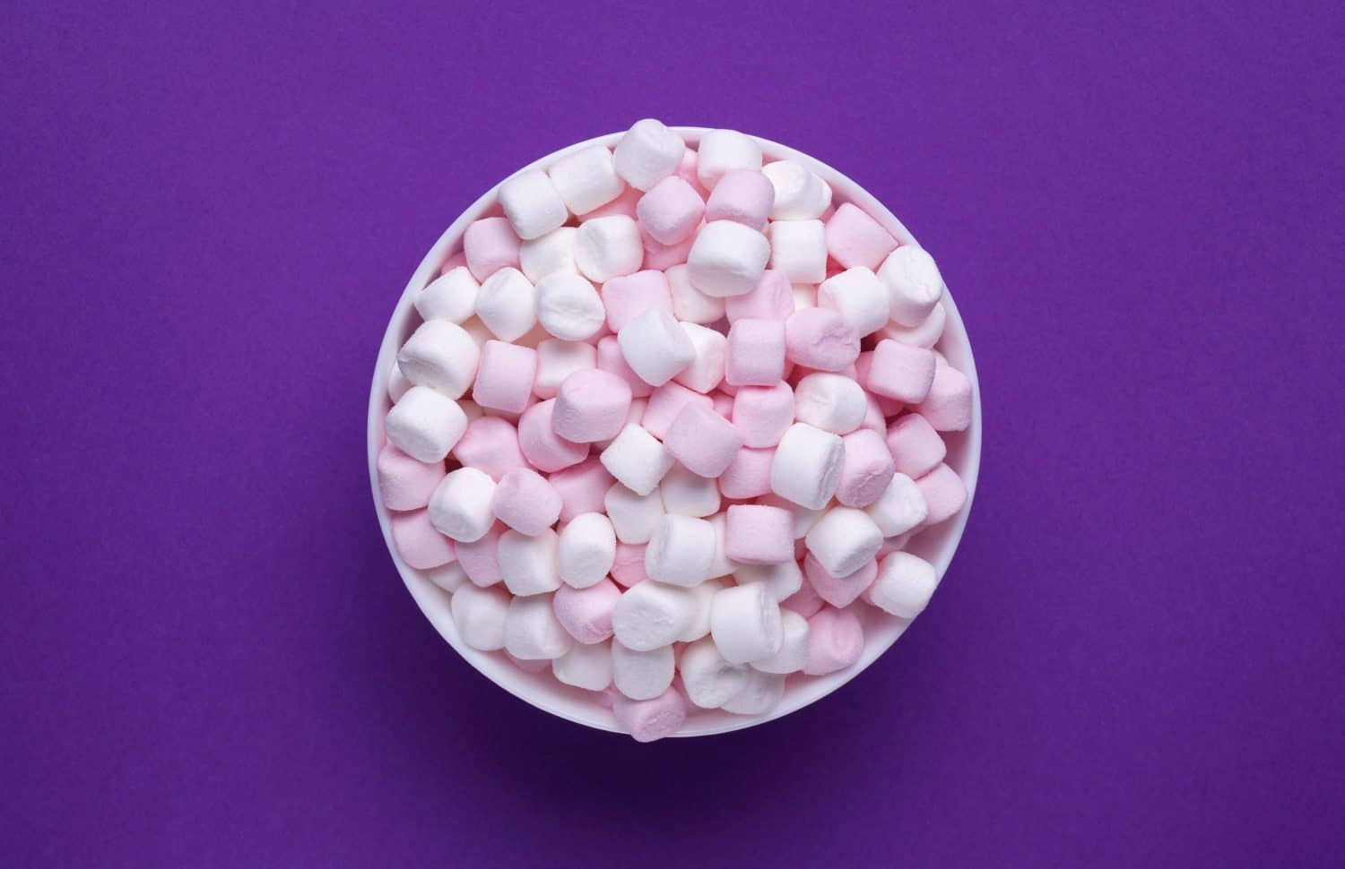 Bowl with delicious marshmallows on purple background, top view