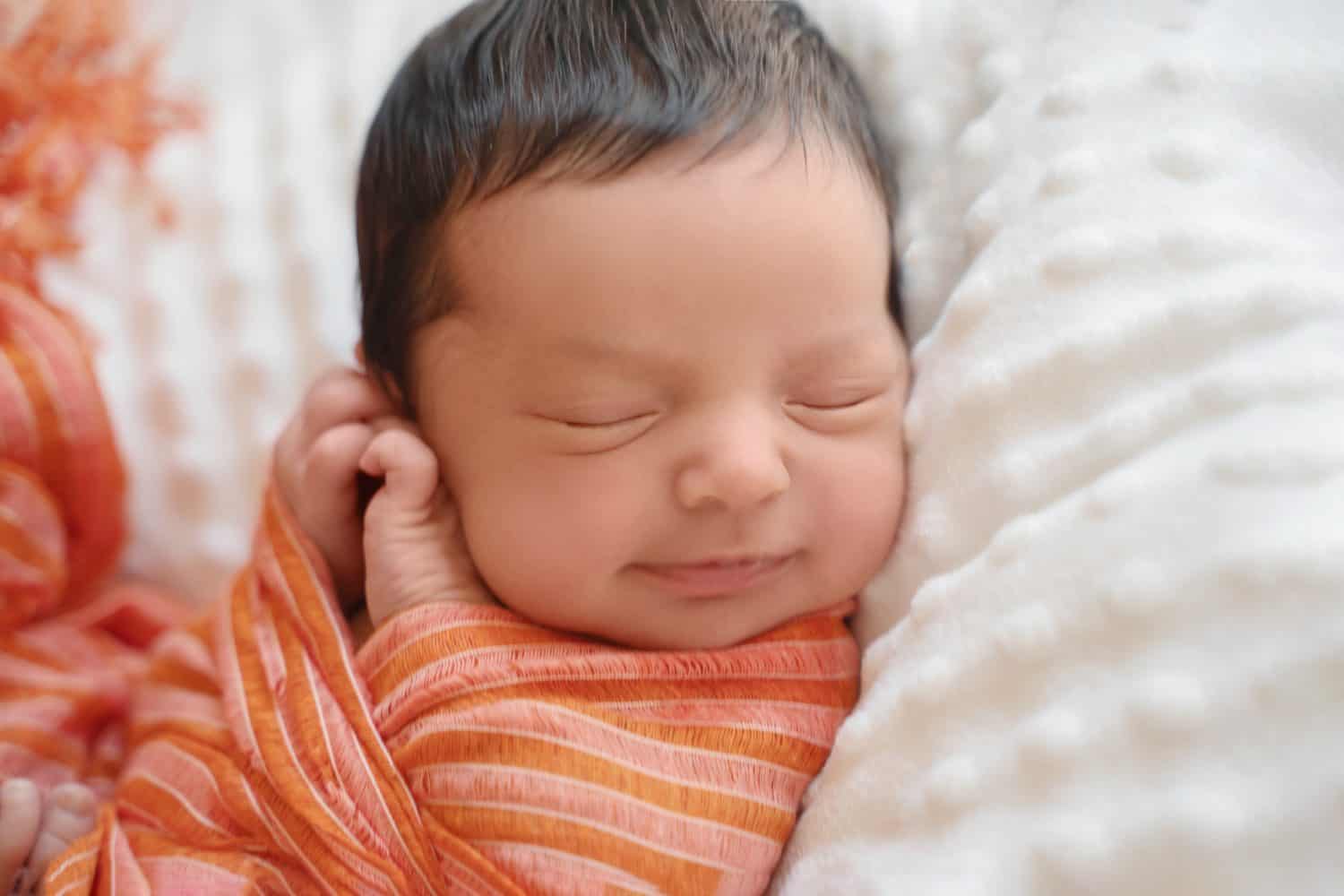 Newborn baby infant with dark hair smiling lying on side sleeping. Cute little Middle eastern child on blanket. Tranquil scene close up