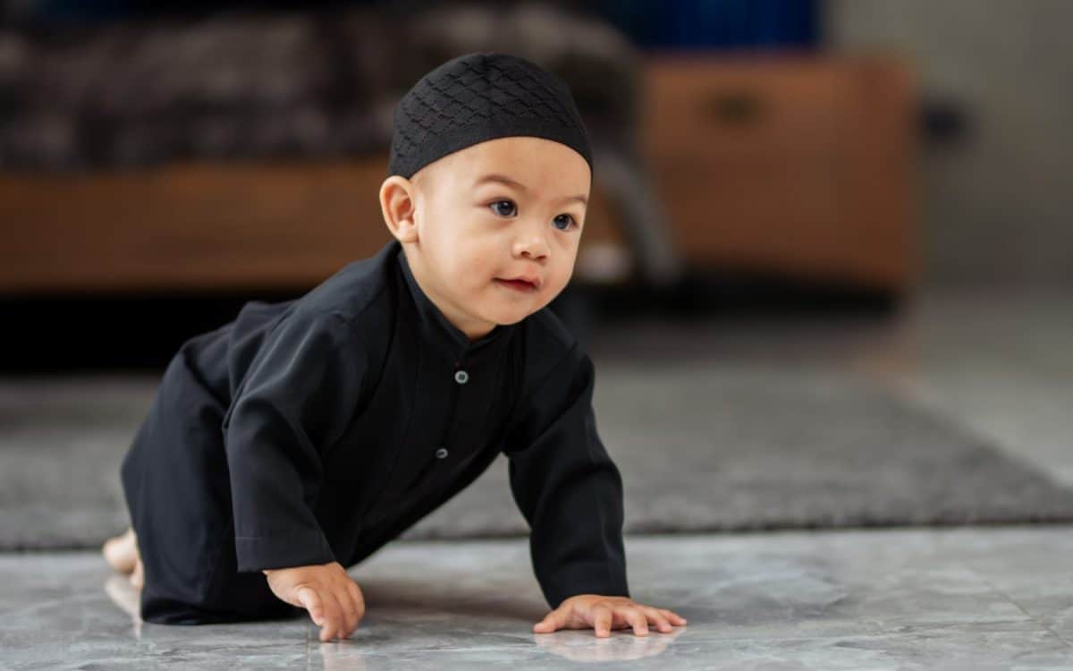 Portrait cute innocent little baby muslim boy wearing traditional clothes, sitting on floor in living room at home, playing alone with copy space. Education, Kid, Religious Concept