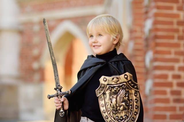 Portrait of a cute little boy dressed as a medieval knight with a sword and a shield. Medieval festival or costume party for kids