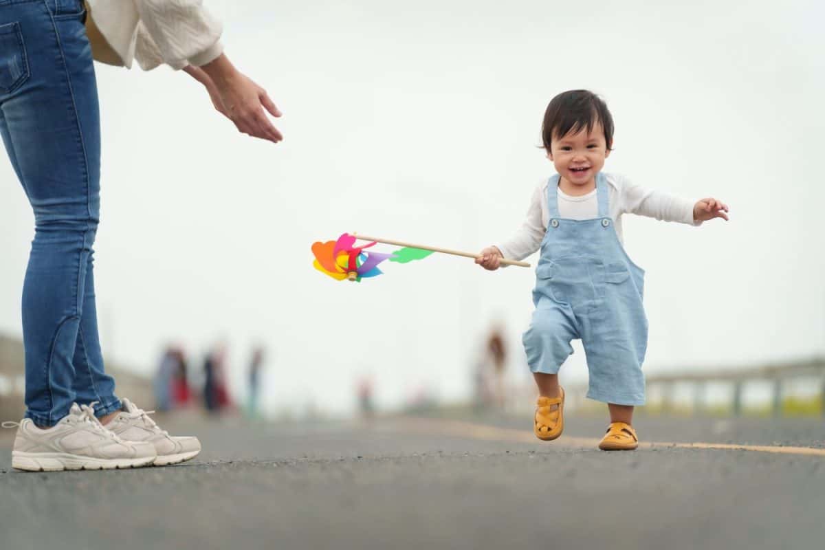 infant baby learn walking first step on a pathway with mother helping